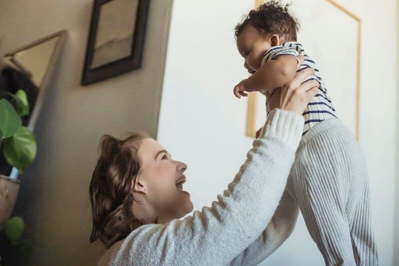 Una madre felice solleva il suo bambino in un ambiente accogliente, celebrando la genitorialità.