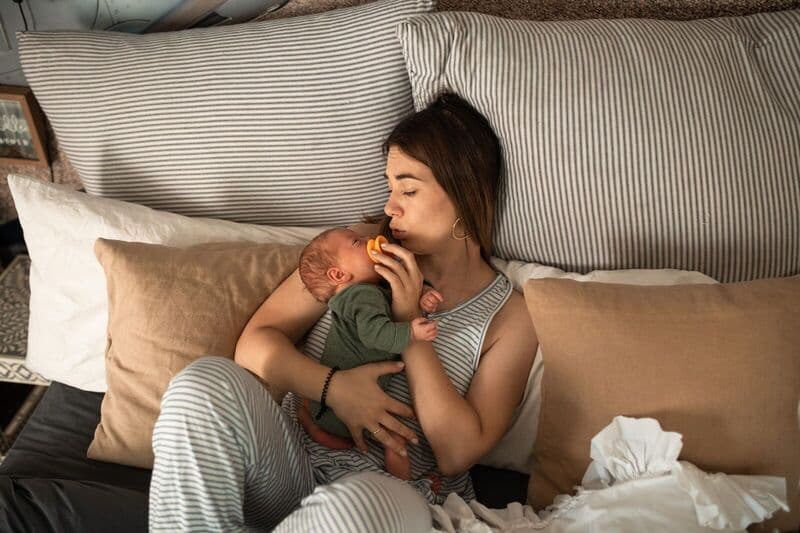 Madre che tiene teneramente il suo neonato mentre si rilassa in una accogliente camera da letto, catturando un momento di calore e cura.