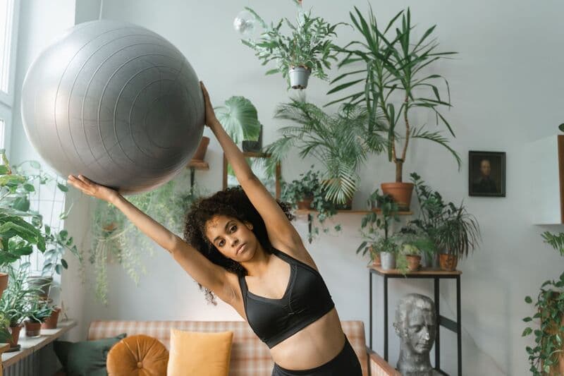 Una donna si allena con una palla fitness circondata da piante verdi da interno, promuovendo uno stile di vita sano.