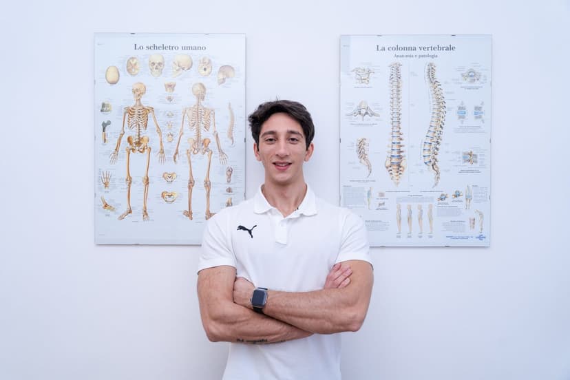Variante praticamente identica del ritratto a braccia incrociate davanti ai poster anatomici, con sorriso appena accennato.