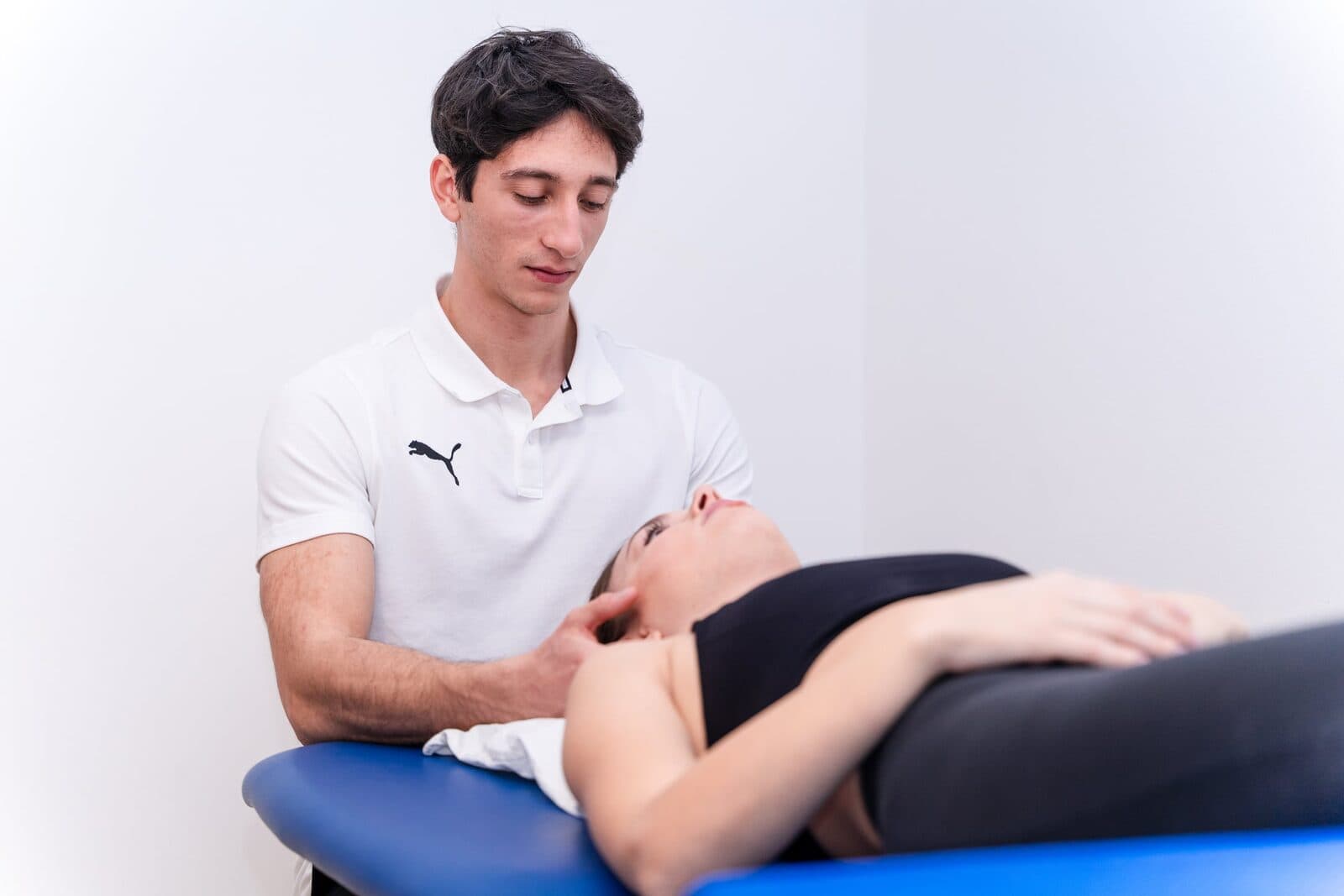 Campo più largo del trattamento cervicale: si vede tutto il lettino blu con la paziente supina e il fisioterapista seduto di lato che lavora sul collo