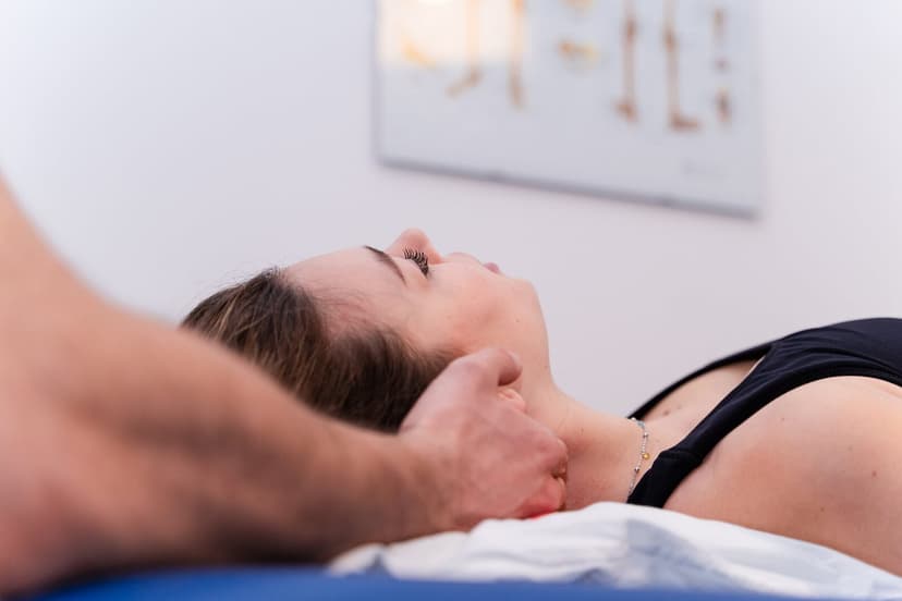 Paziente supina con la testa reclinata all'indietro e le mani del fisioterapista sotto la nuca, poster anatomico sfocato in alto a destra