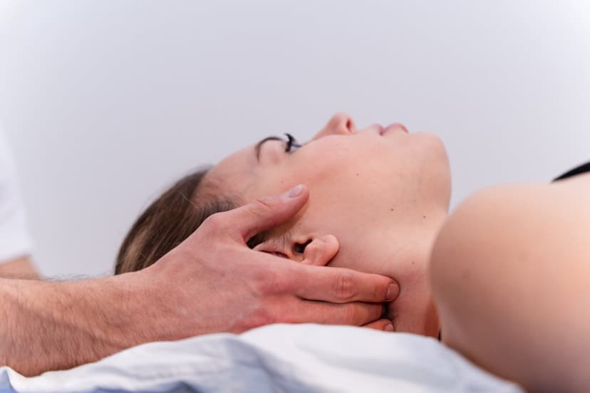 Primissimo piano del collo della paziente distesa con le mani del fisioterapista che sostengono mandibola e cervicale, sfondo bianco