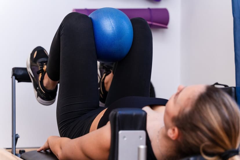 Primo piano delle gambe piegate della paziente che stringe la palla blu tra le ginocchia mentre è distesa sul lettino, testa reclinata sullo sfondo sf