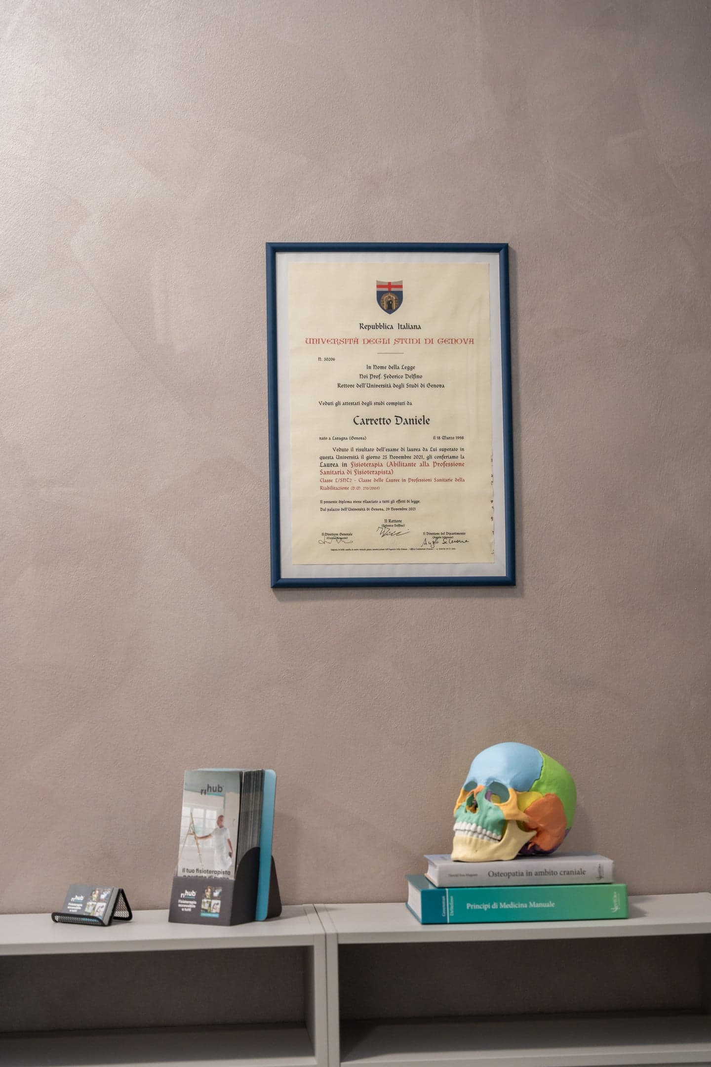 Il diploma di laurea incorniciato appeso alla parete dello studio, sopra un mobile con i libri di medicina.