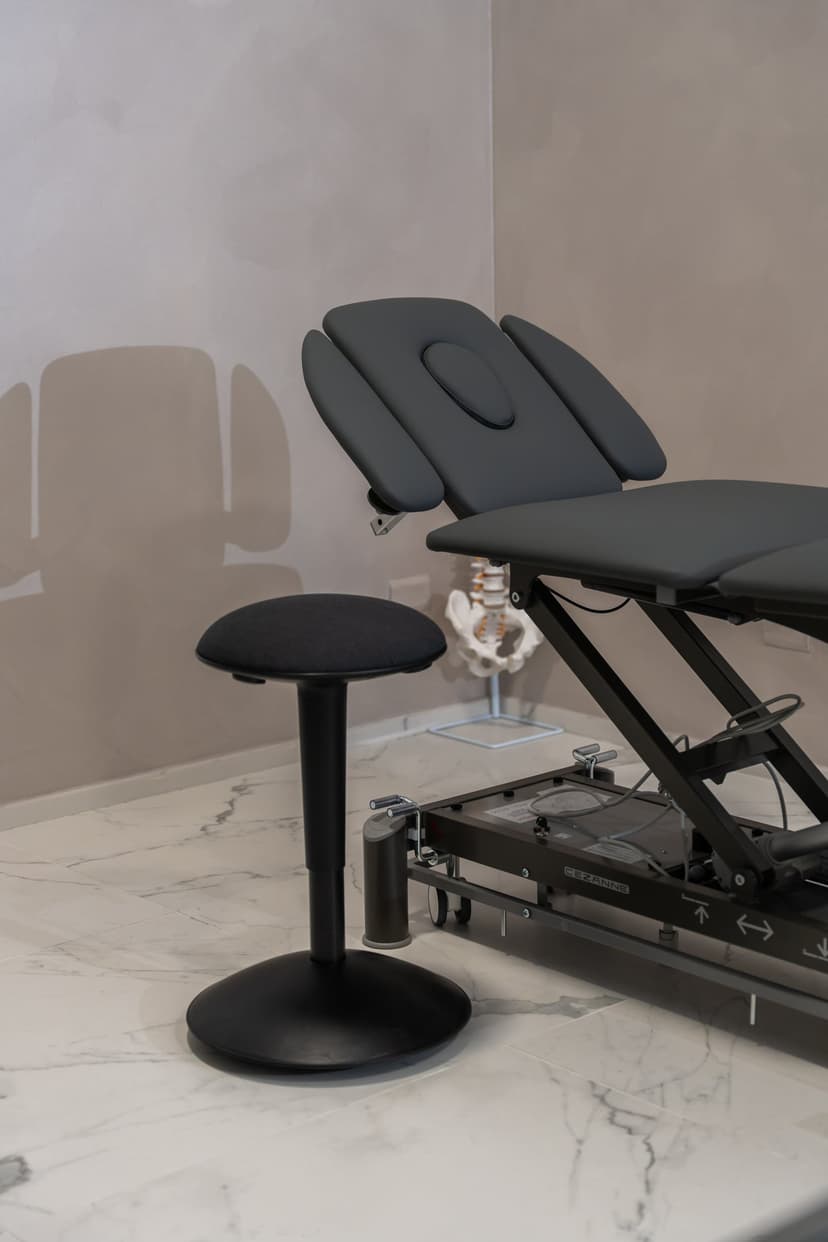 Dettaglio della sala trattamenti: sgabello ergonomico, lettino e modello anatomico di bacino e colonna.
