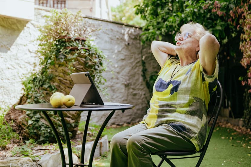 Una signora anziana seduta su una sedia in giardino si allunga con le braccia davanti a sé.