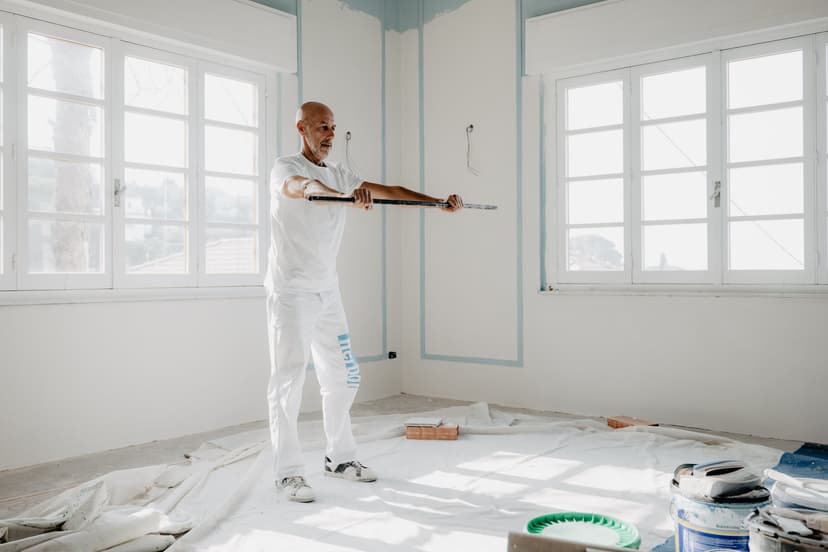 Un uomo in tuta da lavoro solleva un bastone sopra la testa nella stanza che sta imbiancando.