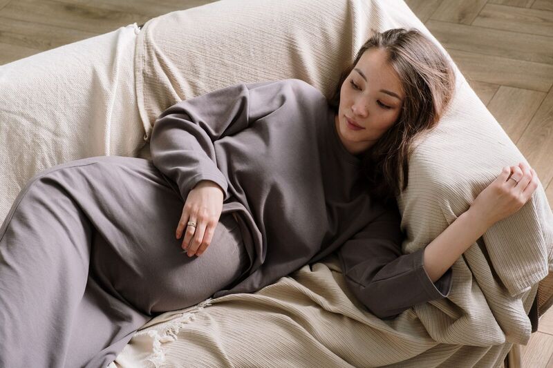 Donna incinta sdraiata su un divano comodo, abbracciando la calma e il relax.